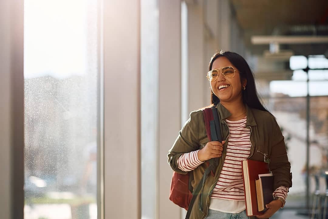 A smiling university student standing in the campus' hallway before her classes start.